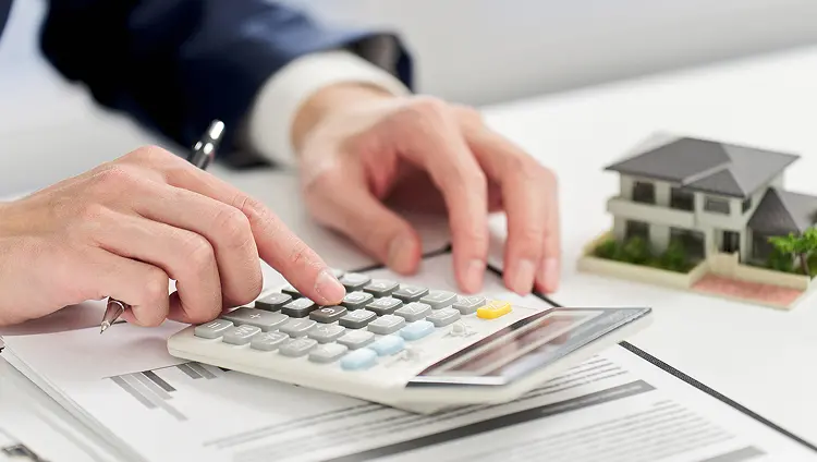 電卓と住宅模型で不動産管理を計算する手元